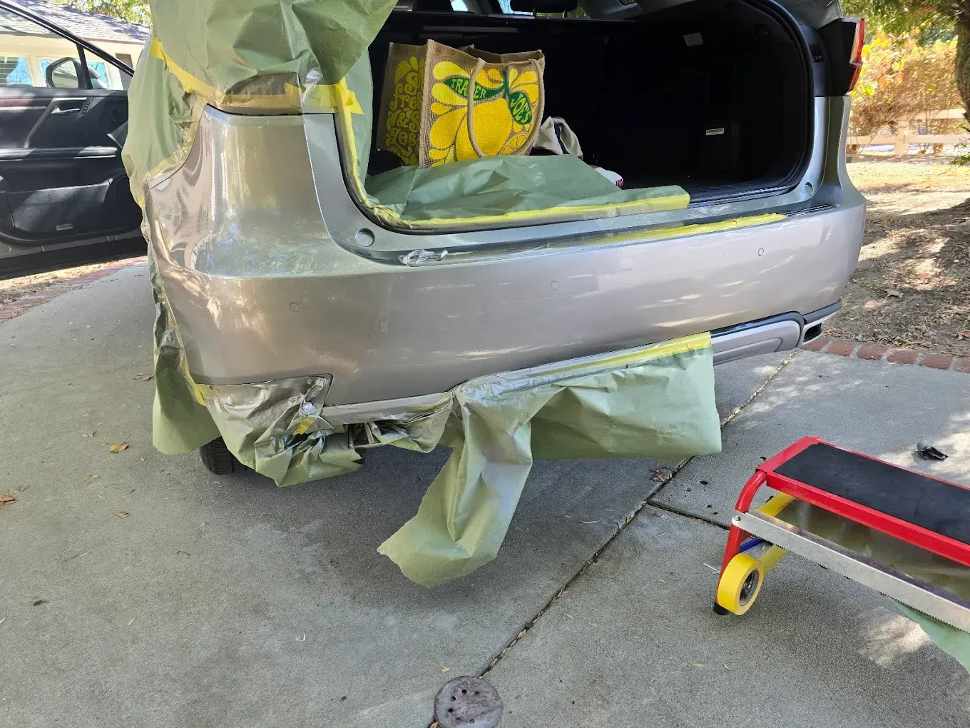 A car with a damaged rear bumper, prepped for repair with masking paper and tape, sitting on a concrete surface outdoors.