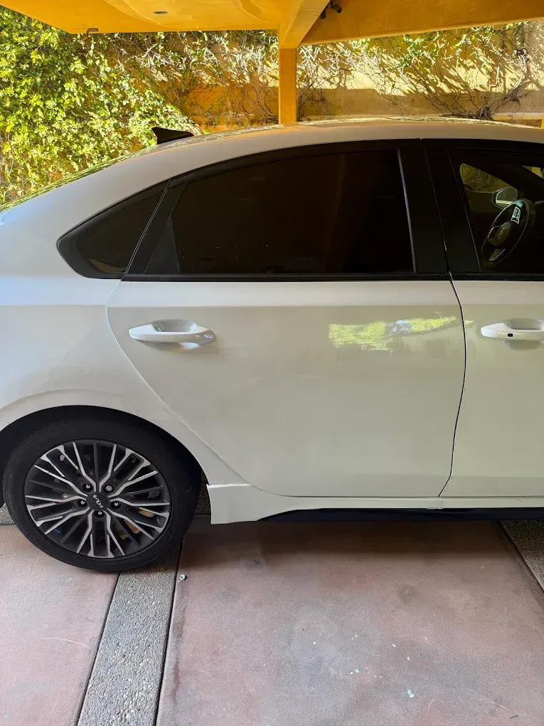 White sedan parked under a carport. The car has tinted windows and black and silver rims.