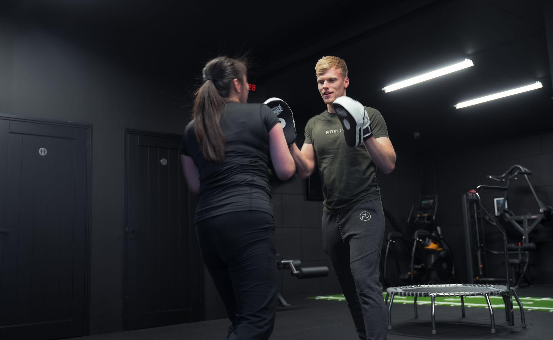 Man en vrouw boksen in een personal training studio. Man in groen shirt geeft een stoot, vrouw in zwart verdedigt.
