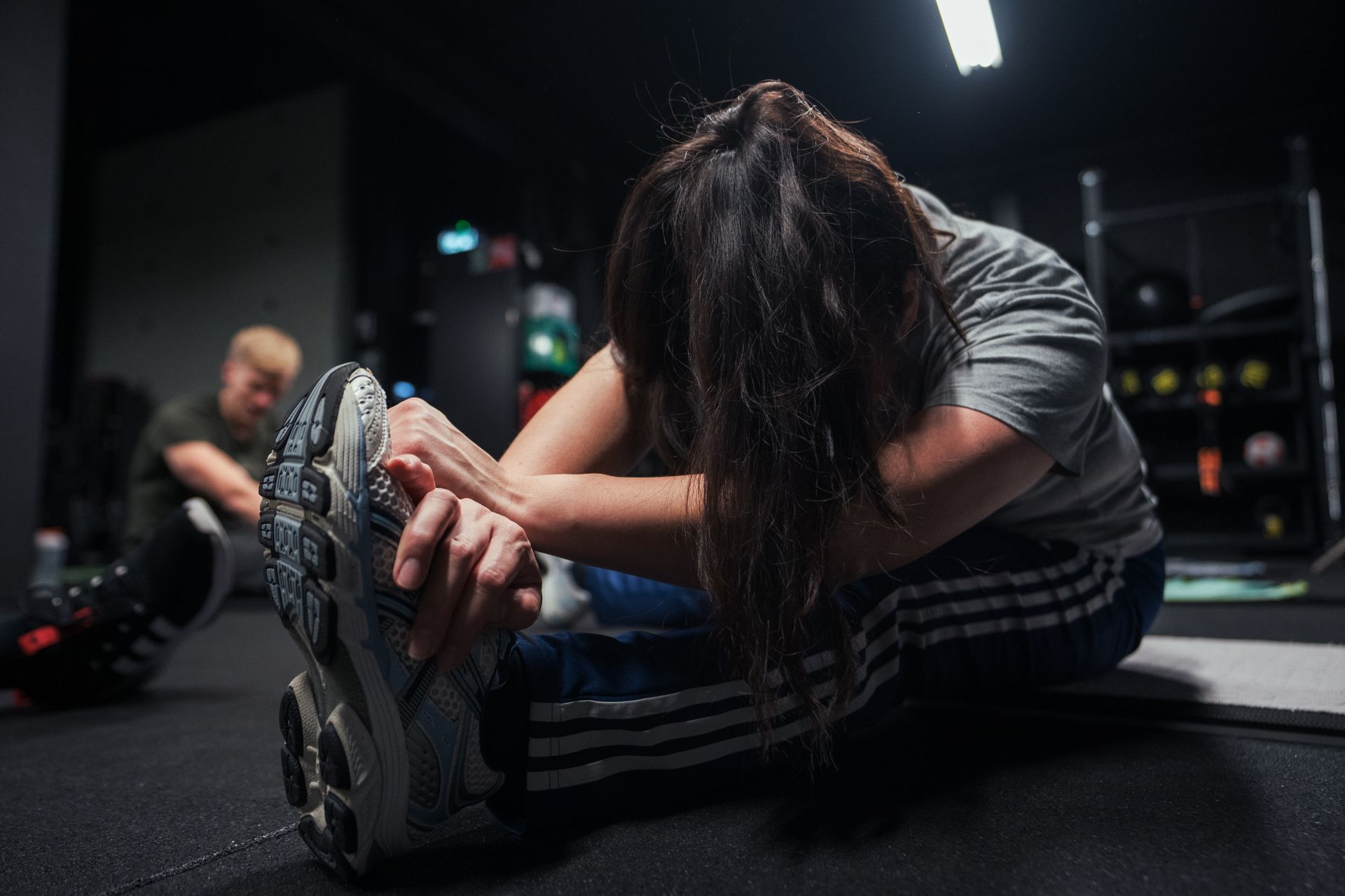Een vrouw strekt haar been in een sportschool; iemand anders op de achtergrond.