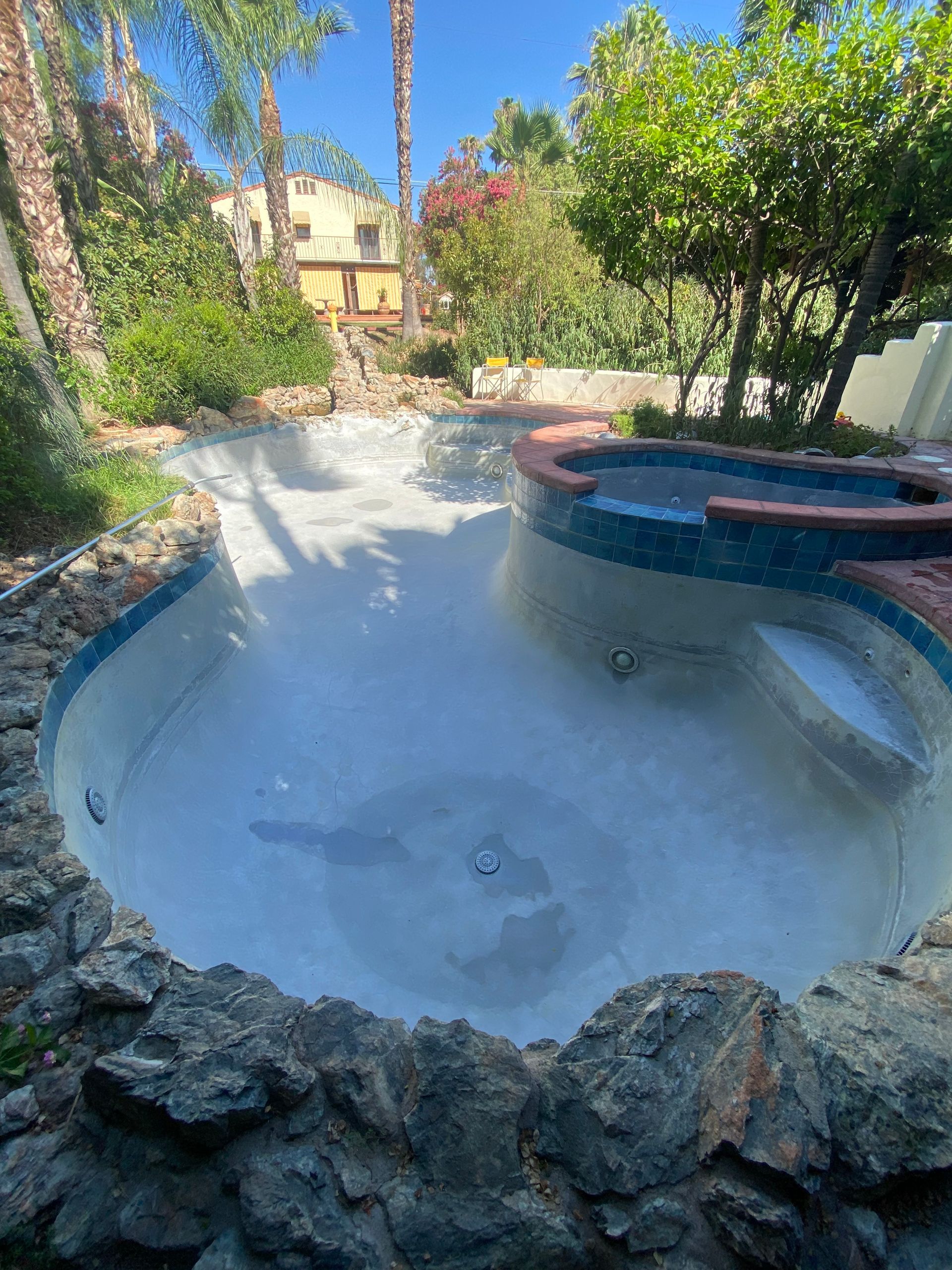 A large swimming pool surrounded by rocks and trees in a backyard.