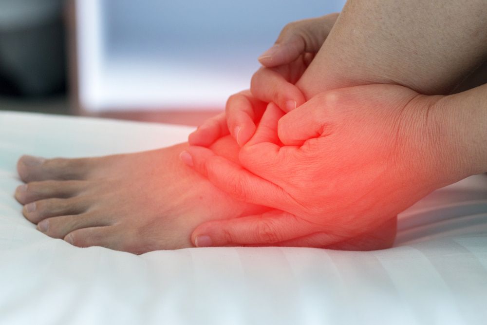 A Person Is Holding Their Foot in Pain on A Bed — Swan Podiatry and Orthotics in Coconut Grove, NT