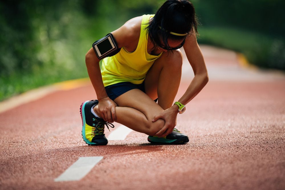 A Woman Is Kneeling Down on A Track Holding Her Knee in Pain — Swan Podiatry and Orthotics in Katherine, NT