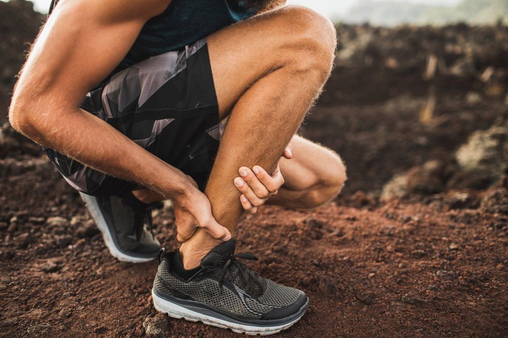 A Man Is Kneeling Down and Holding His Ankle in Pain — Swan Podiatry and Orthotics in Coconut Grove, NT