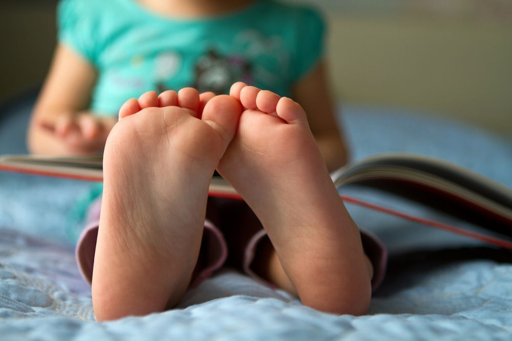 A Little Girl Is Sitting on A Bed Reading a Book — Swan Podiatry and Orthotics in Coconut Grove, NT