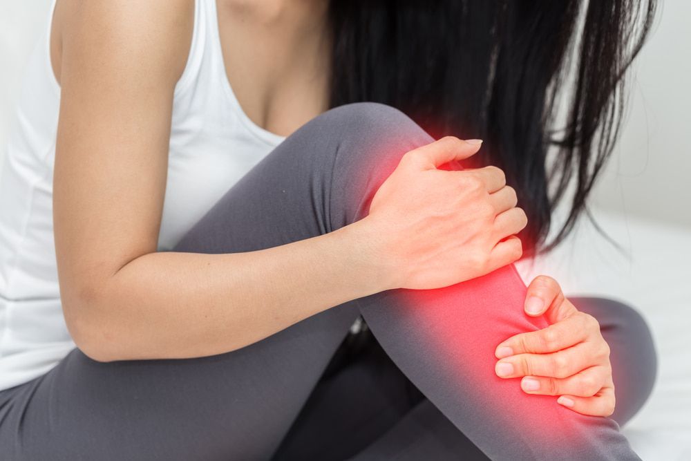 A Woman Is Sitting on The Floor Holding Her Knee in Pain — Swan Podiatry and Orthotics in Coconut Grove, NT