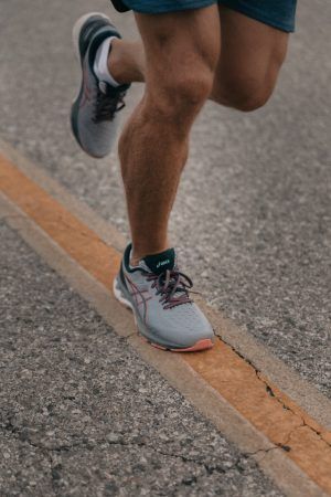 A Person Is Running on A Road Wearing Asics Shoes — Swan Podiatry and Orthotics in Coconut Grove, NT