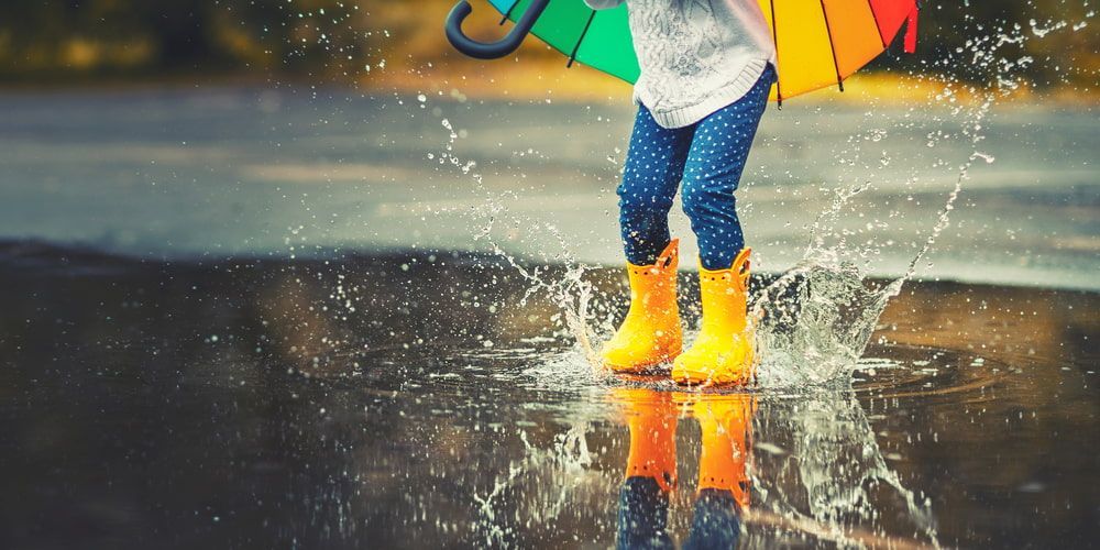 A Little Girl Is Jumping in A Puddle with An Umbrella — Swan Podiatry and Orthotics in Katherine, NT