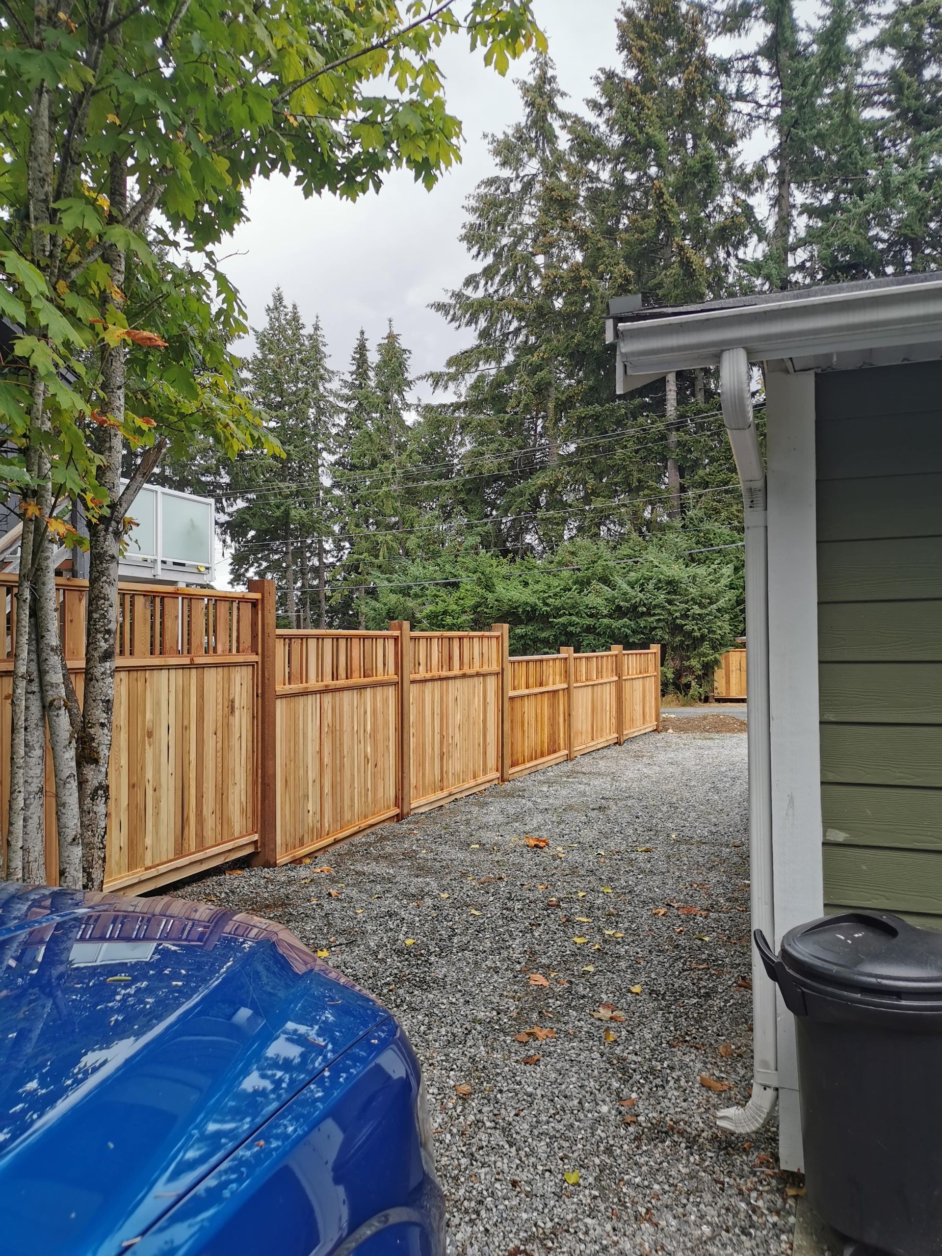 A blue car is parked in front of a wooden fence.