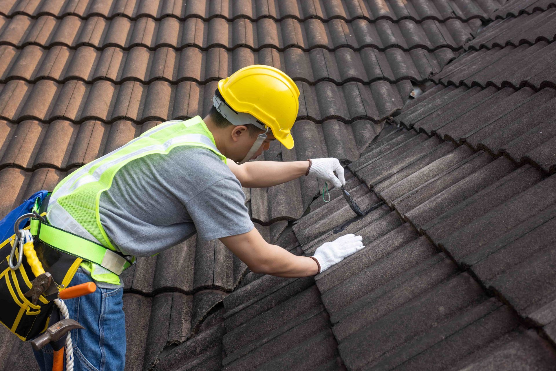 A man wearing a hard hat and safety vest is working on a roof.