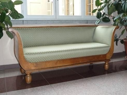 Divano antico in legno con rivestimento a fantasia verde chiaro, vicino a una finestra.