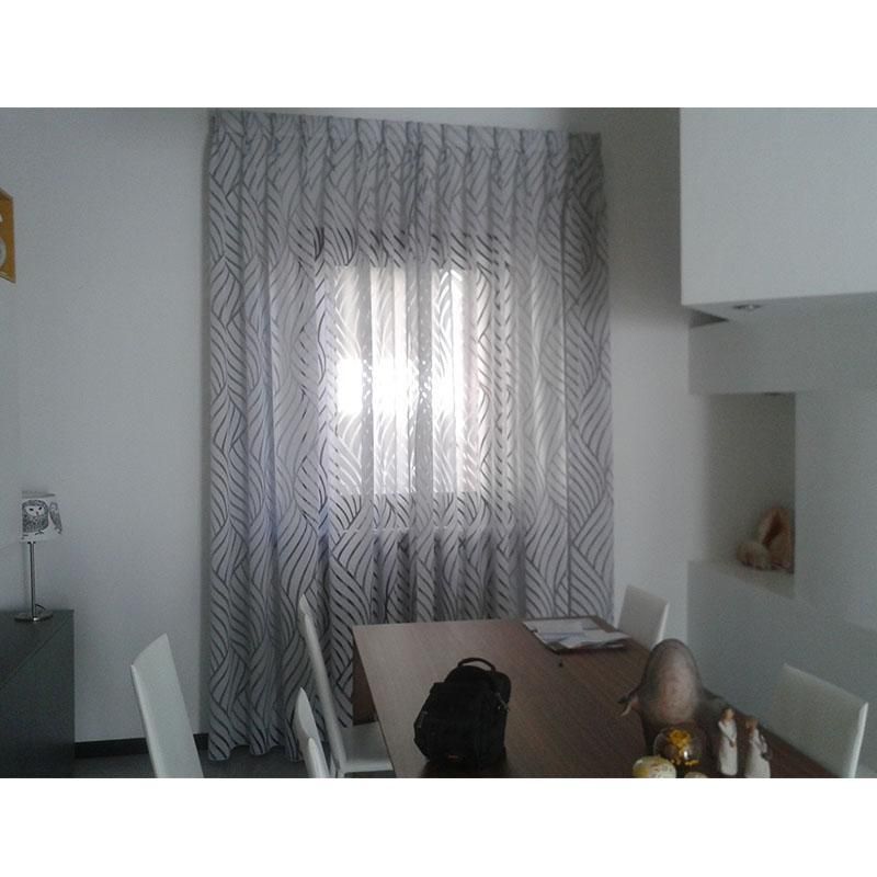 Una sala da pranzo con una finestra coperta da tende a fantasia, un tavolo con sedie e pareti bianche.