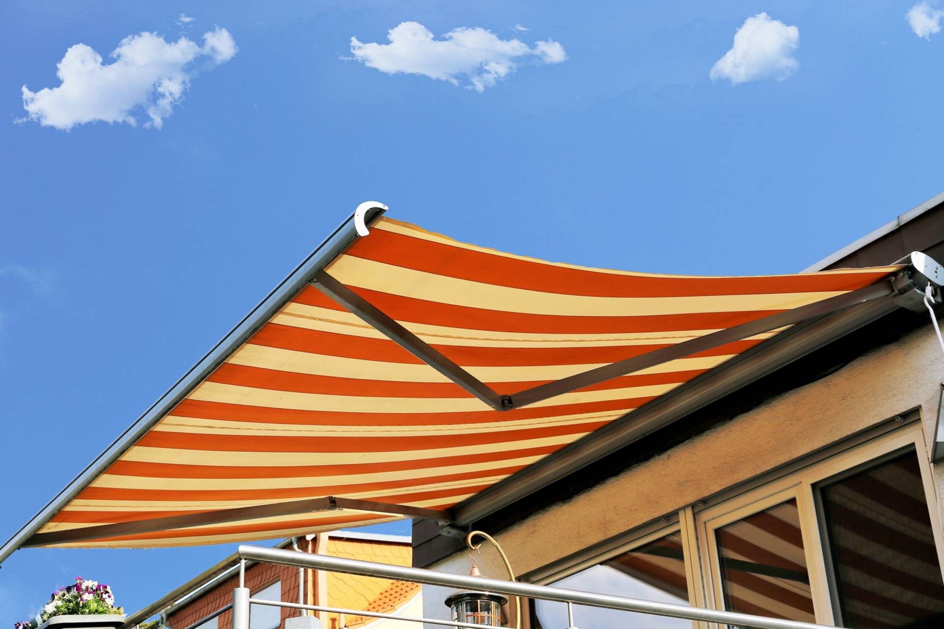 Una tenda a strisce arancioni e crema si estende da un balcone sotto un cielo azzurro brillante con nuvole.