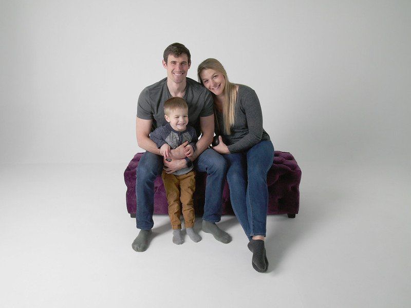 A family is posing for a picture while sitting on a purple ottoman.