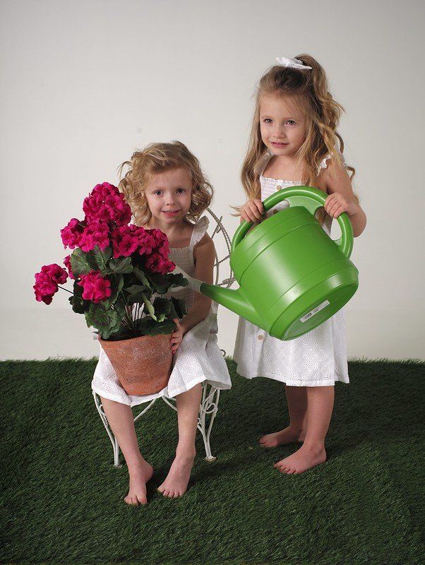 Two little girls holding a green watering can and a potted plant