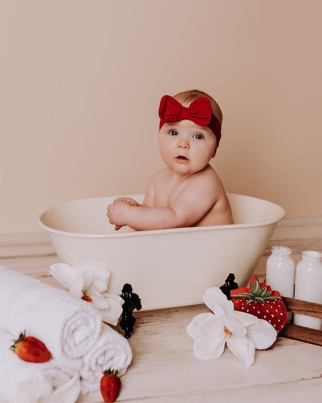 A baby is sitting in a bathtub surrounded by towels and strawberries.
