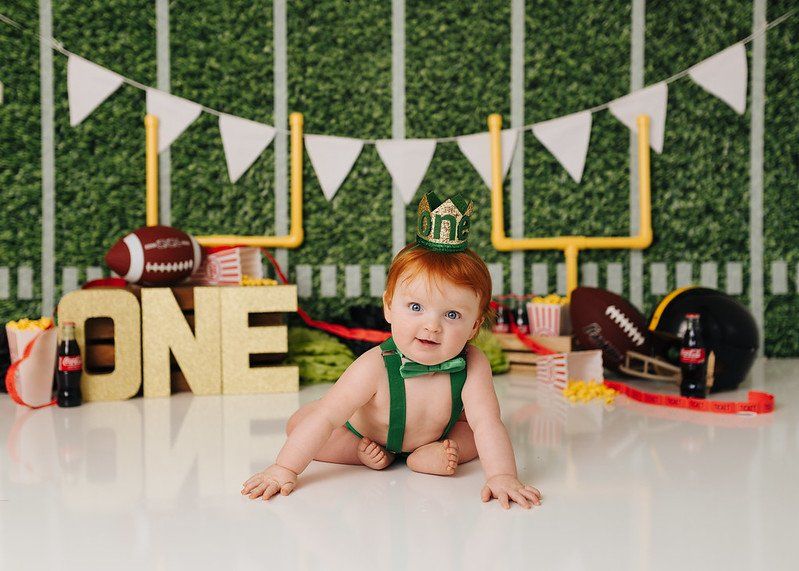A baby is sitting on the floor in front of a football field.