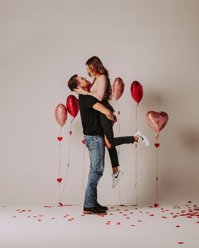 A man is holding a woman in his arms in front of balloons.