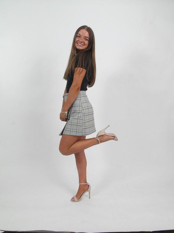 A woman in a plaid skirt and heels is standing on one leg.