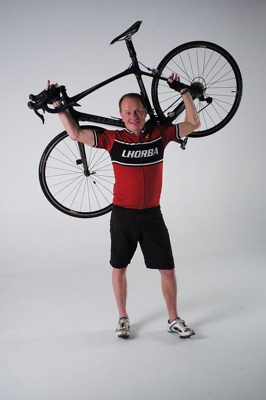 A man in a red shirt is holding a bicycle over his head.