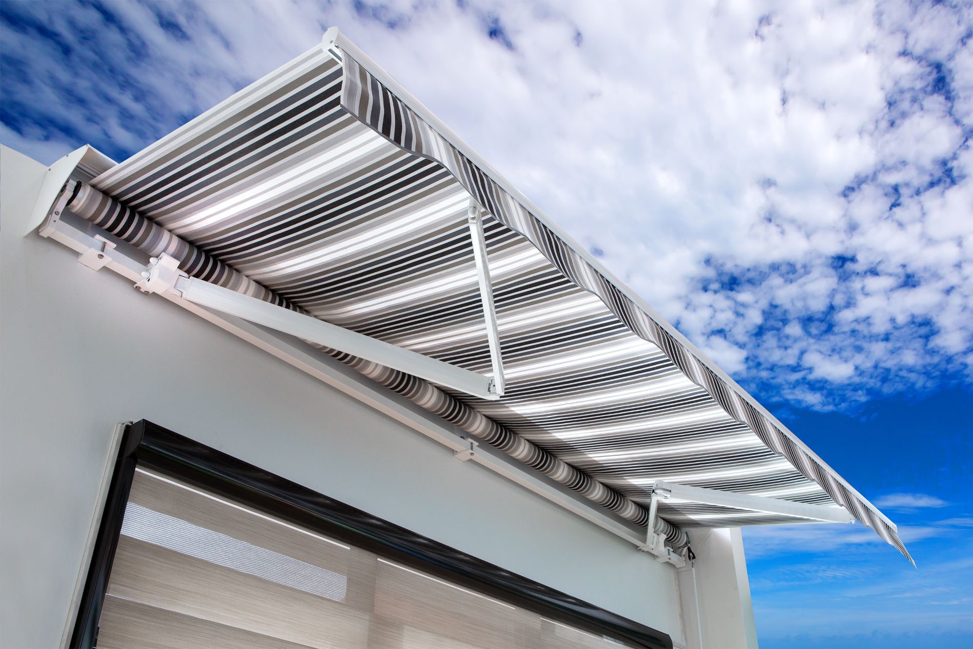 Tenda da sole bianca a lamelle sopra la finestra di un edificio, contro un cielo azzurro con nuvole.