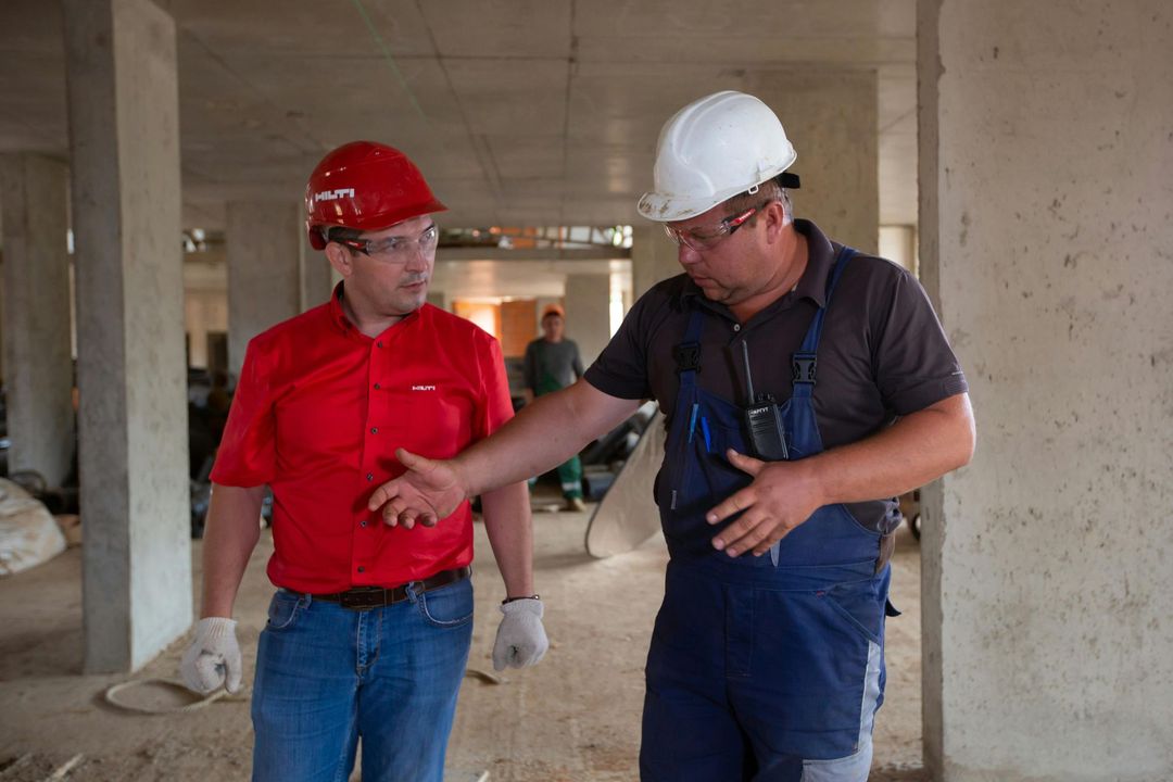Two construction workers are talking to each other in a building under construction.