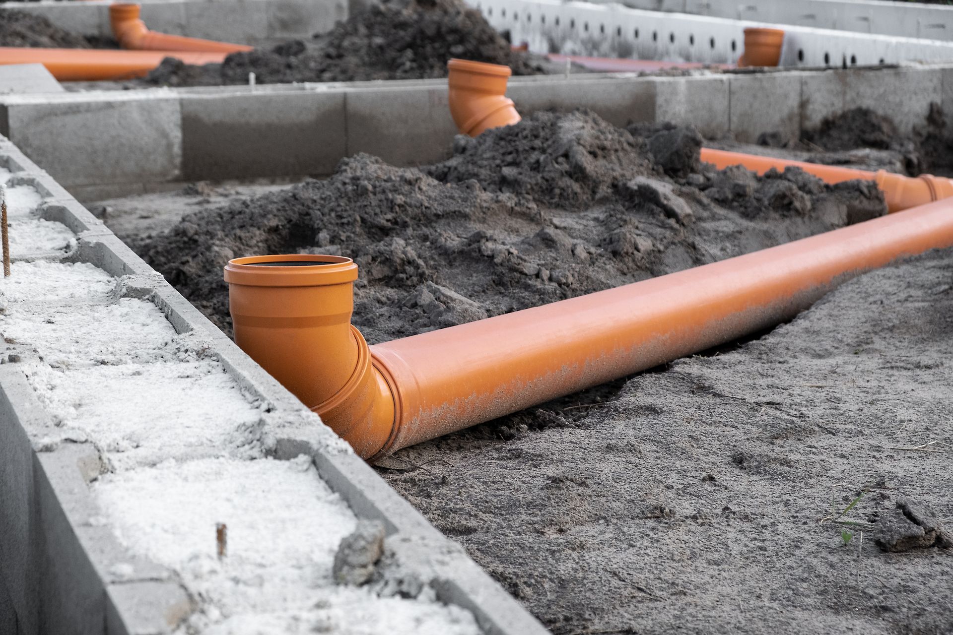 A bunch of pipes are laying in the dirt on a construction site.