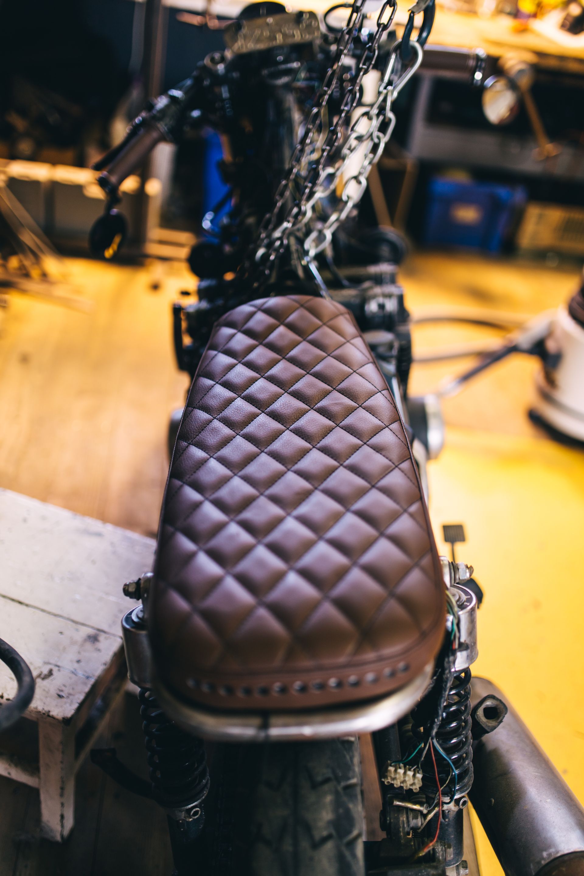 A close up of a motorcycle with a quilted seat in a garage.