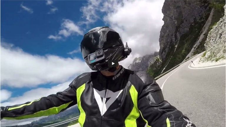 Helmeted motorcyclist riding on a winding mountain road with cliffs and blue sky