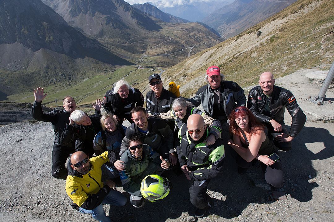 Group of hikers posing on a rocky mountain trail with backpacks and helmets, smiling in the sun