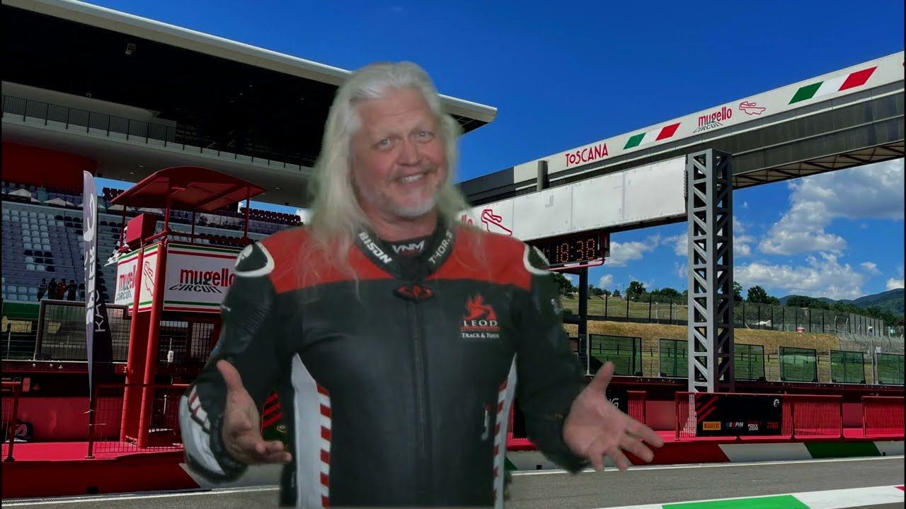 Smiling driver in black and red racing suit standing in a racetrack pit area