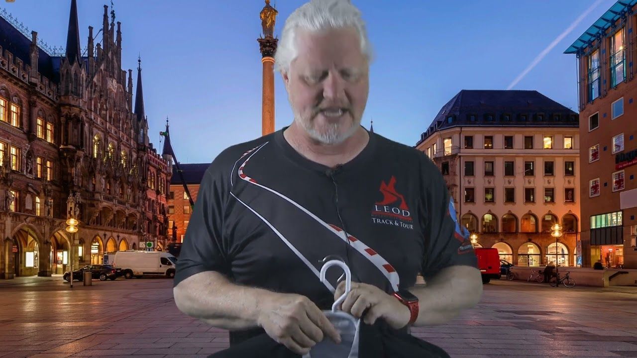 Man holding a rope in a city square at dusk, with lit historic buildings in the background