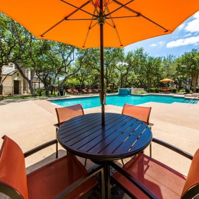 a table and chairs under an orange umbrella next to a swimming pool .