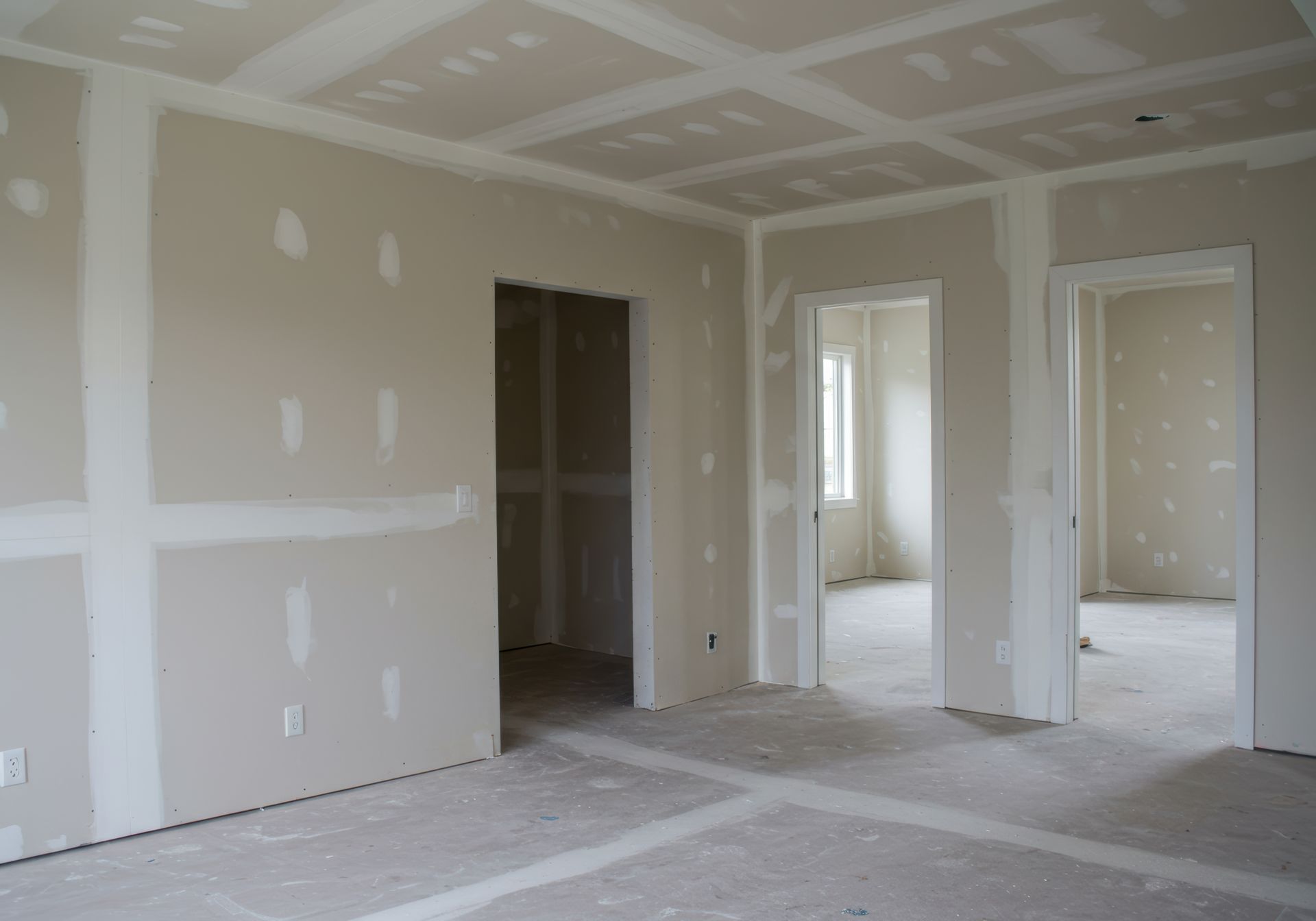 Interior view of a room under construction; drywall walls and ceiling with open doorways.