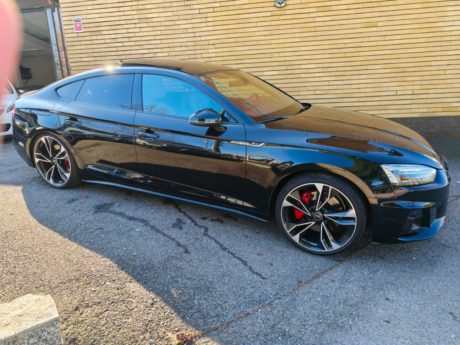Audi A5 Sportback nera parcheggiata su una superficie asfaltata con pinze dei freni rosse visibili dietro le ruote.