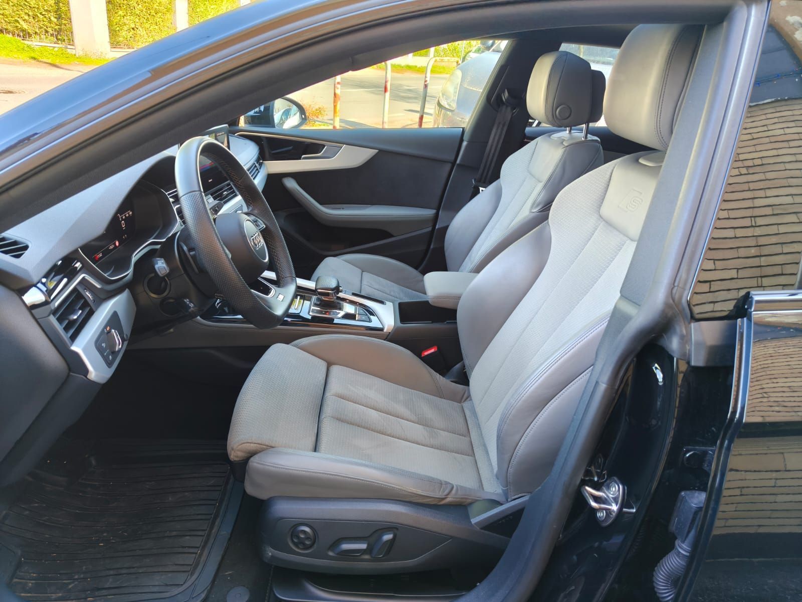 Interno di un'Audi nera con sedili in pelle grigia. La portiera lato guida è aperta.