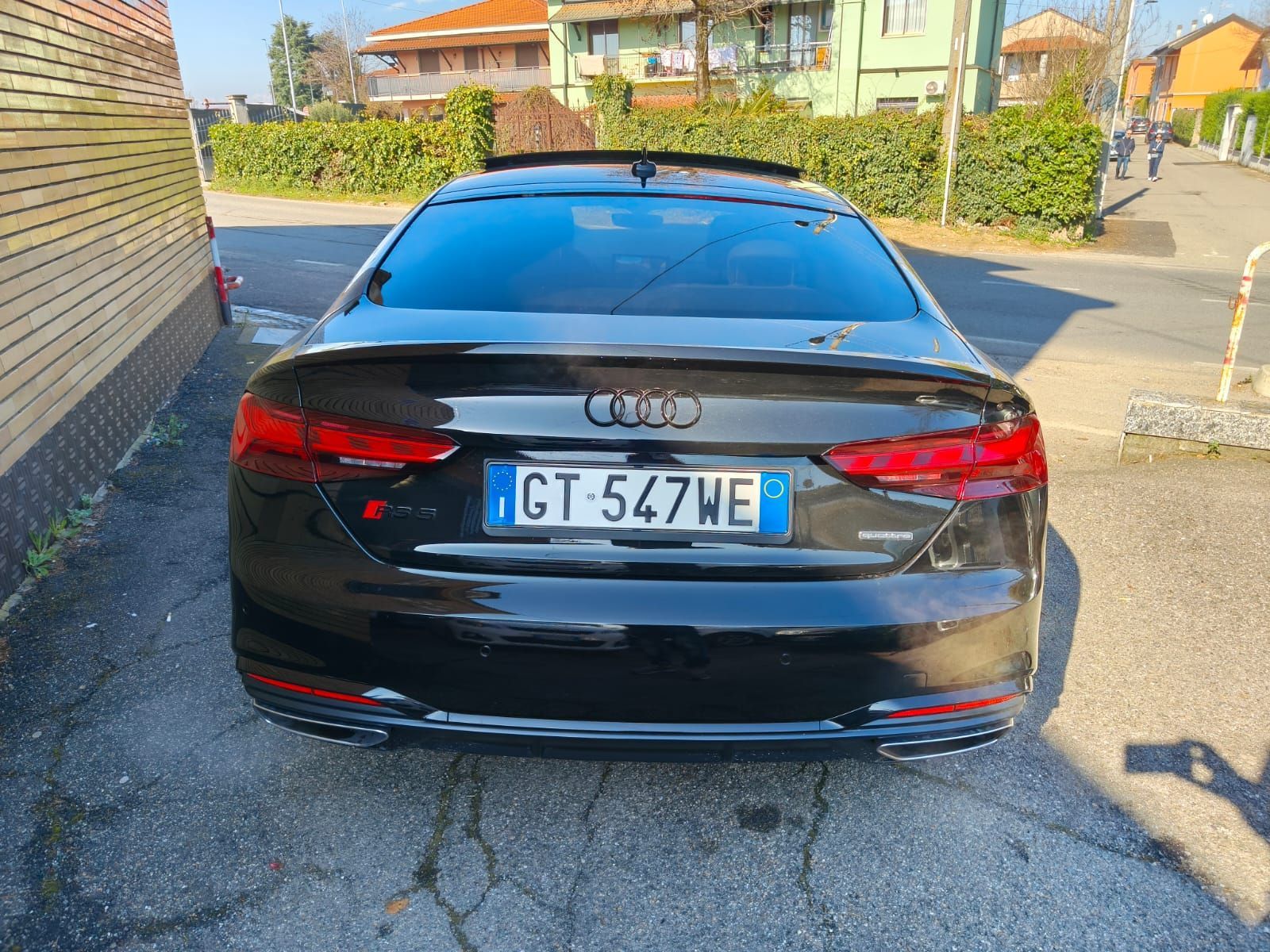 Berlina Audi nera con targa italiana GT 547WE parcheggiata su una strada.
