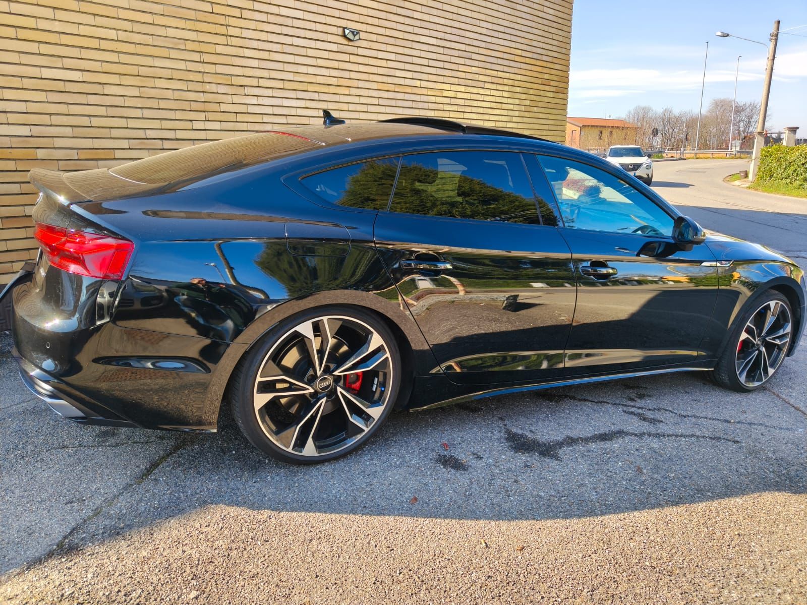 Un'Audi coupé nera parcheggiata su una strada asfaltata accanto a un edificio in mattoni.
