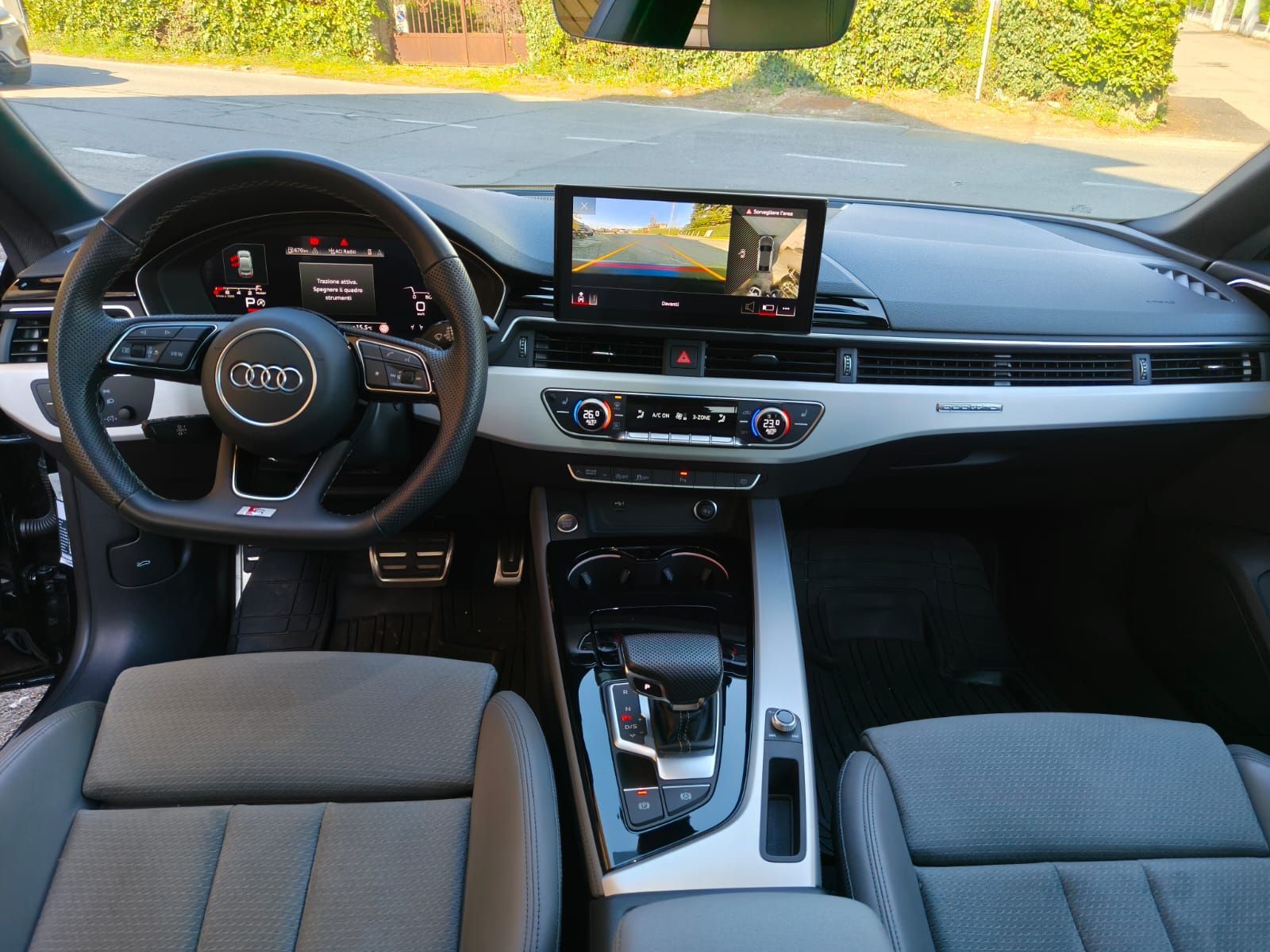 Vista interna del cruscotto di un'auto Audi con volante, schermo e console centrale.