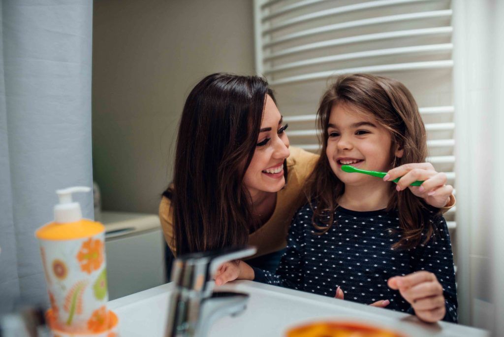Mother helping brush little girl's teeth | Home dental care