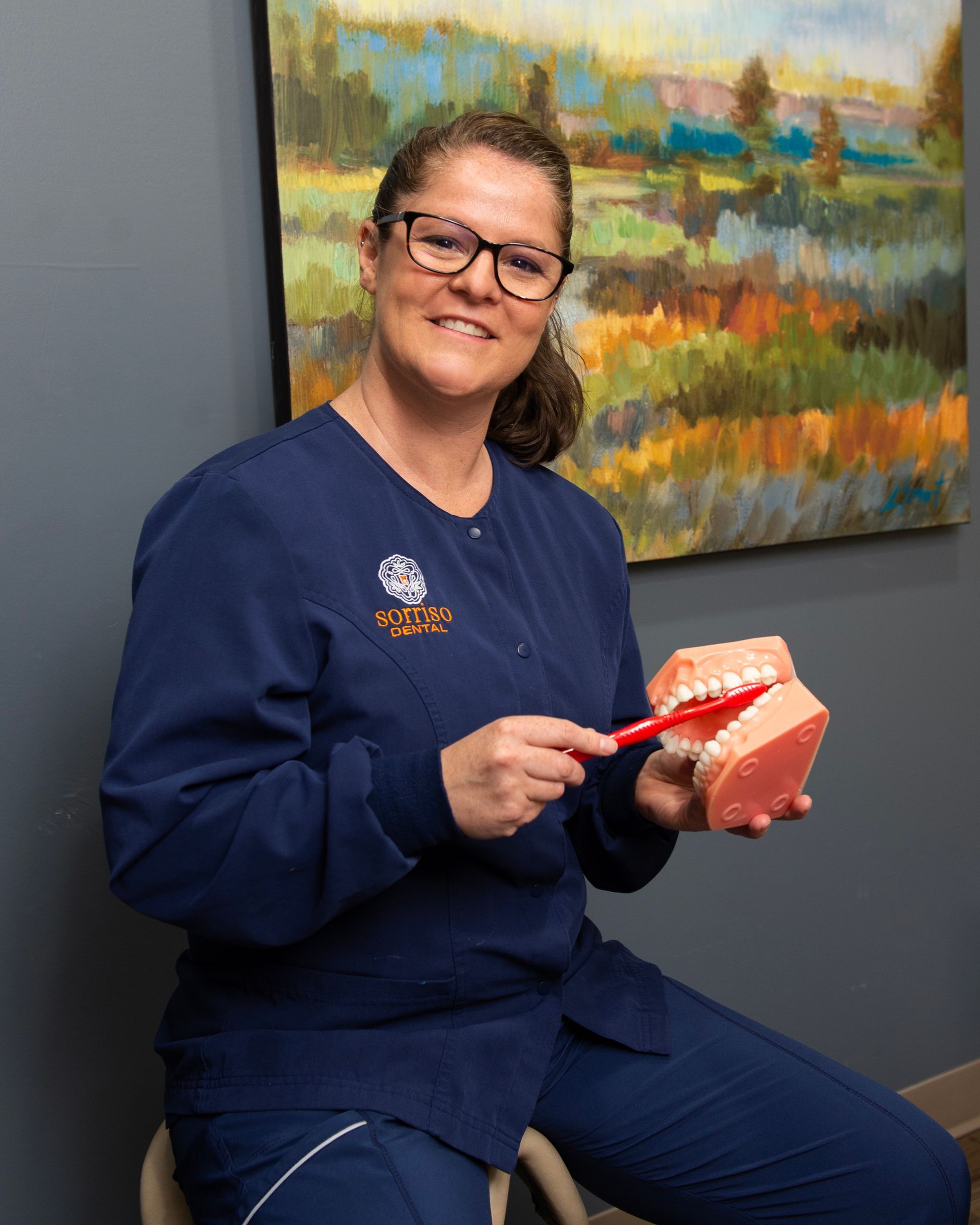 A woman is sitting on a chair holding a model of teeth and a toothbrush.