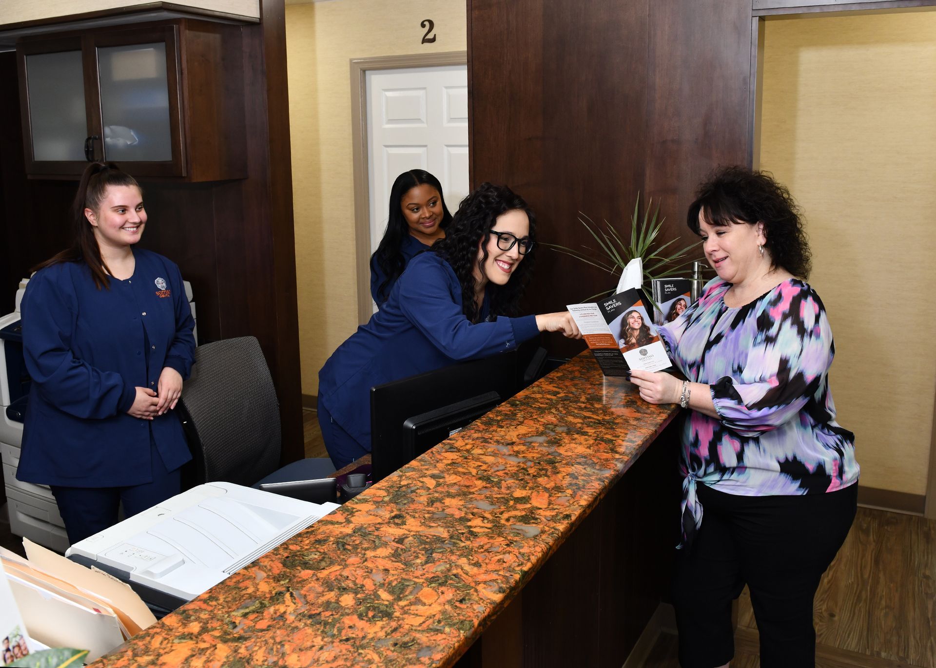 A group of women are standing around a counter in a dental office.