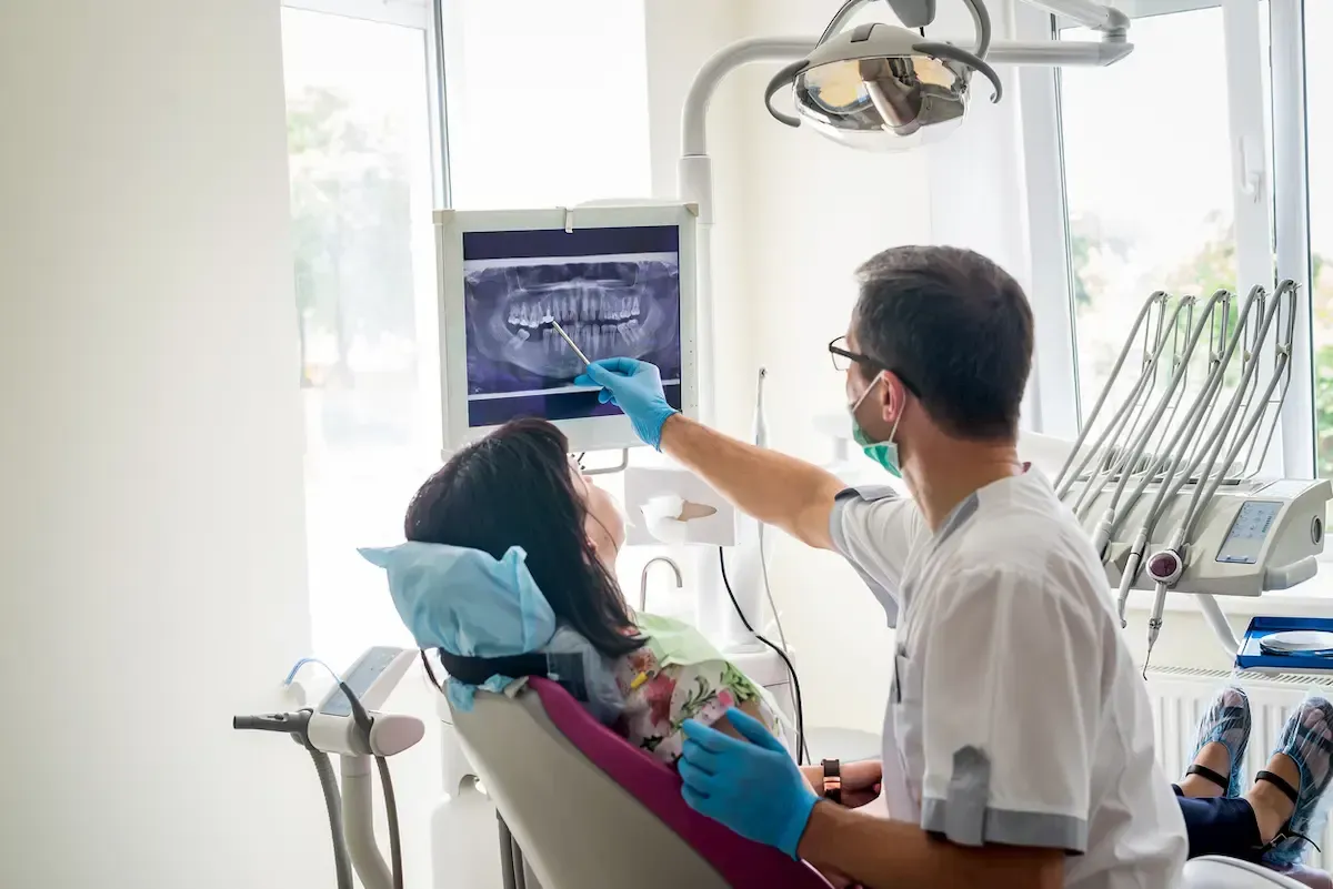 Dentist pointing at an x-ray of teeth, explaining the image to a patient in a dental office.