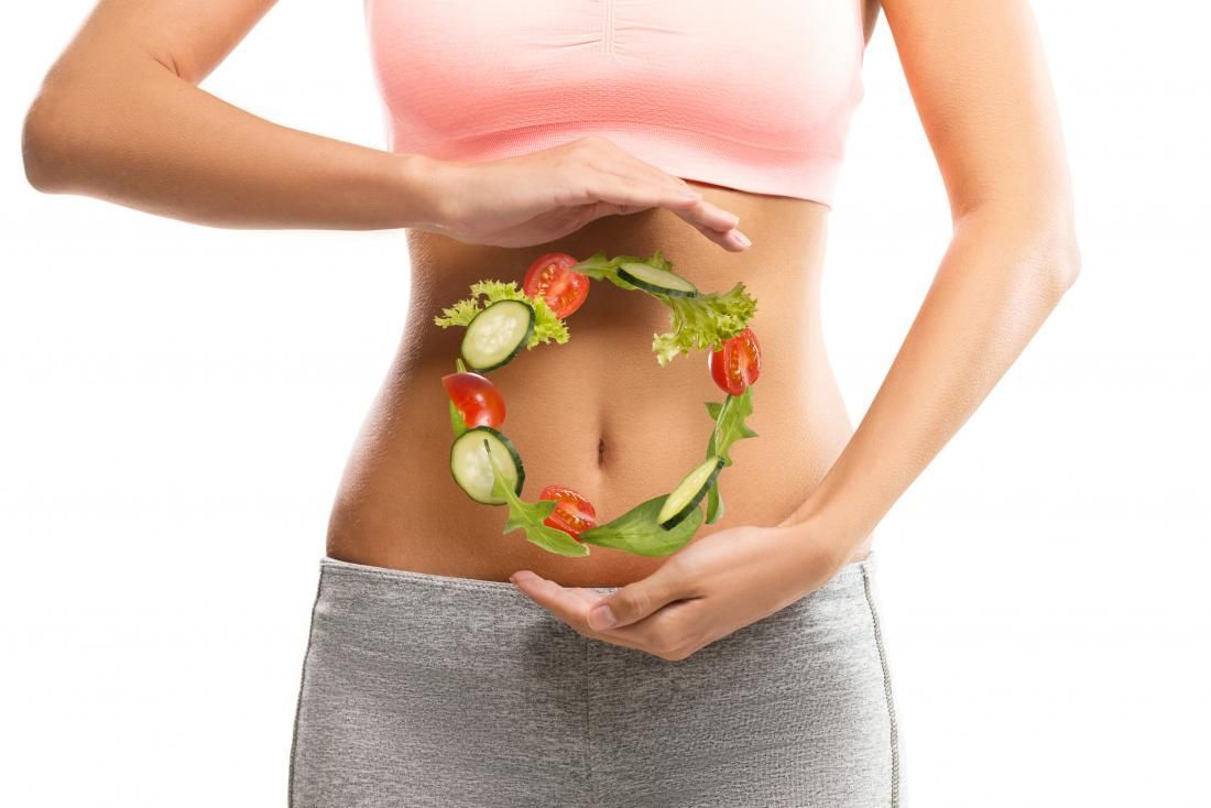 A woman is holding a wreath of vegetables around her stomach.