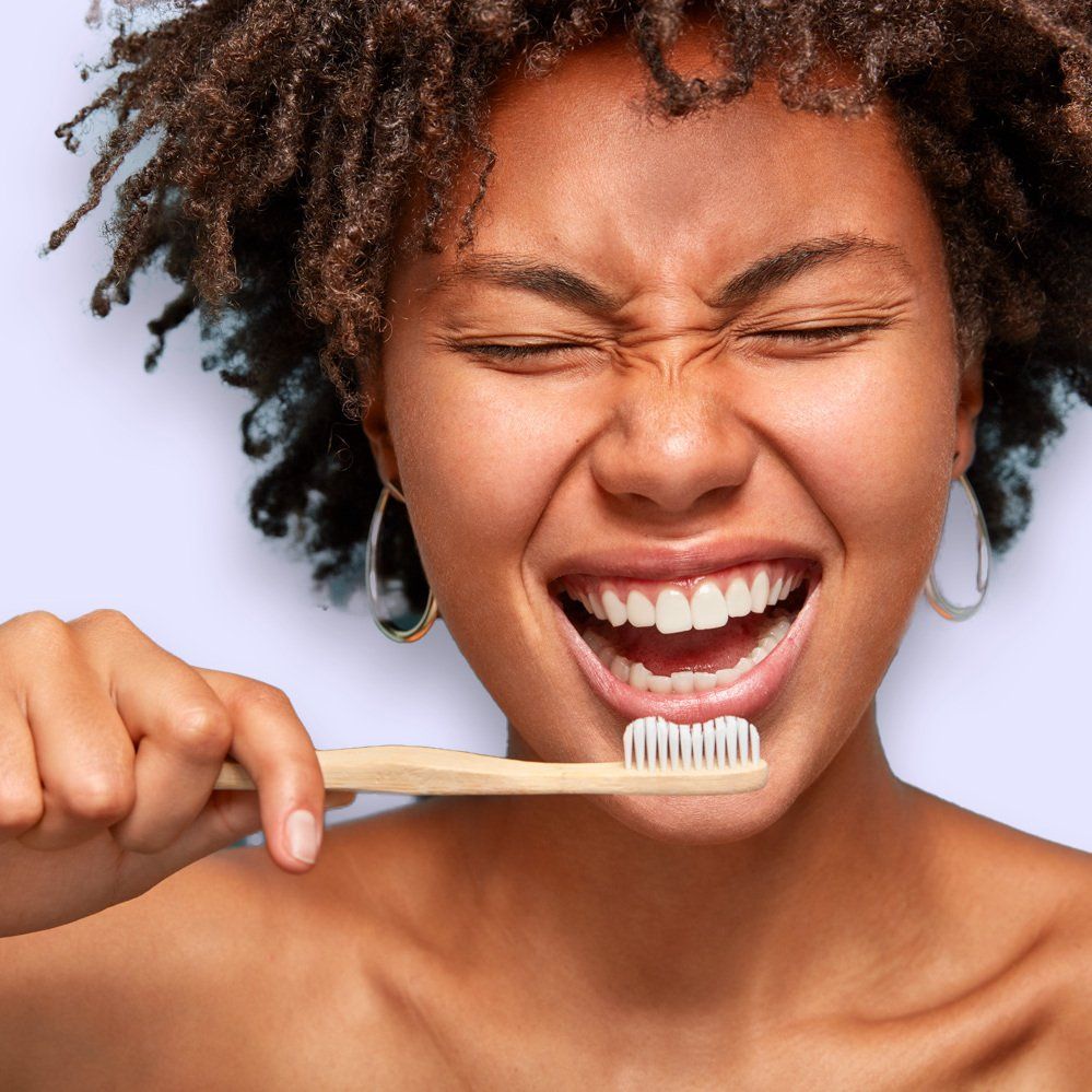 A woman is smiling while brushing her teeth with a toothbrush