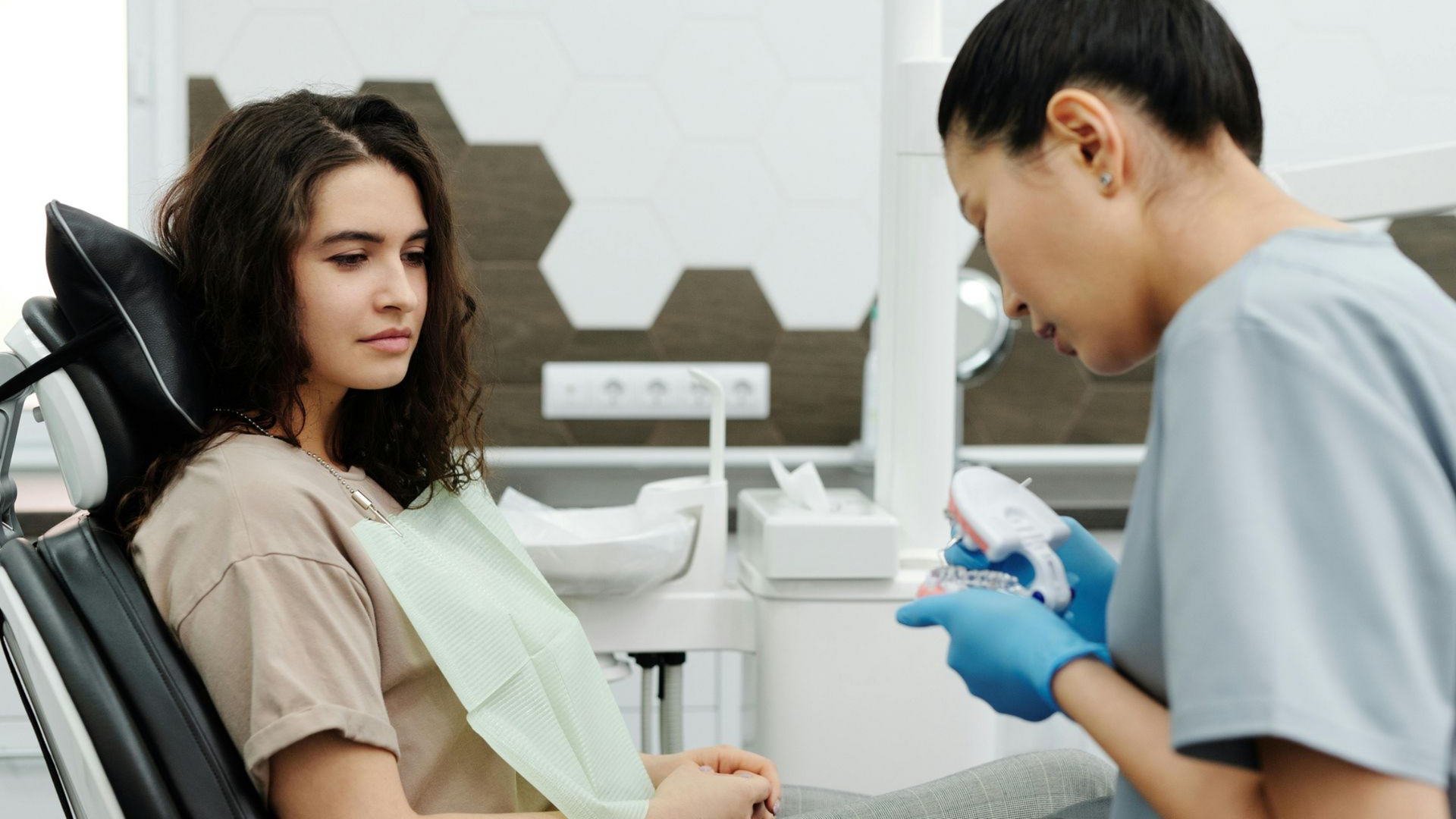 Dentist holding a model of teeth, showing a patient and discussing the details of the treatment
