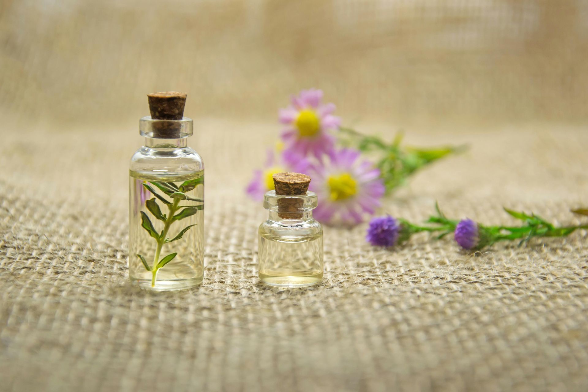 Two bottles of essential oil with flowers in the background.