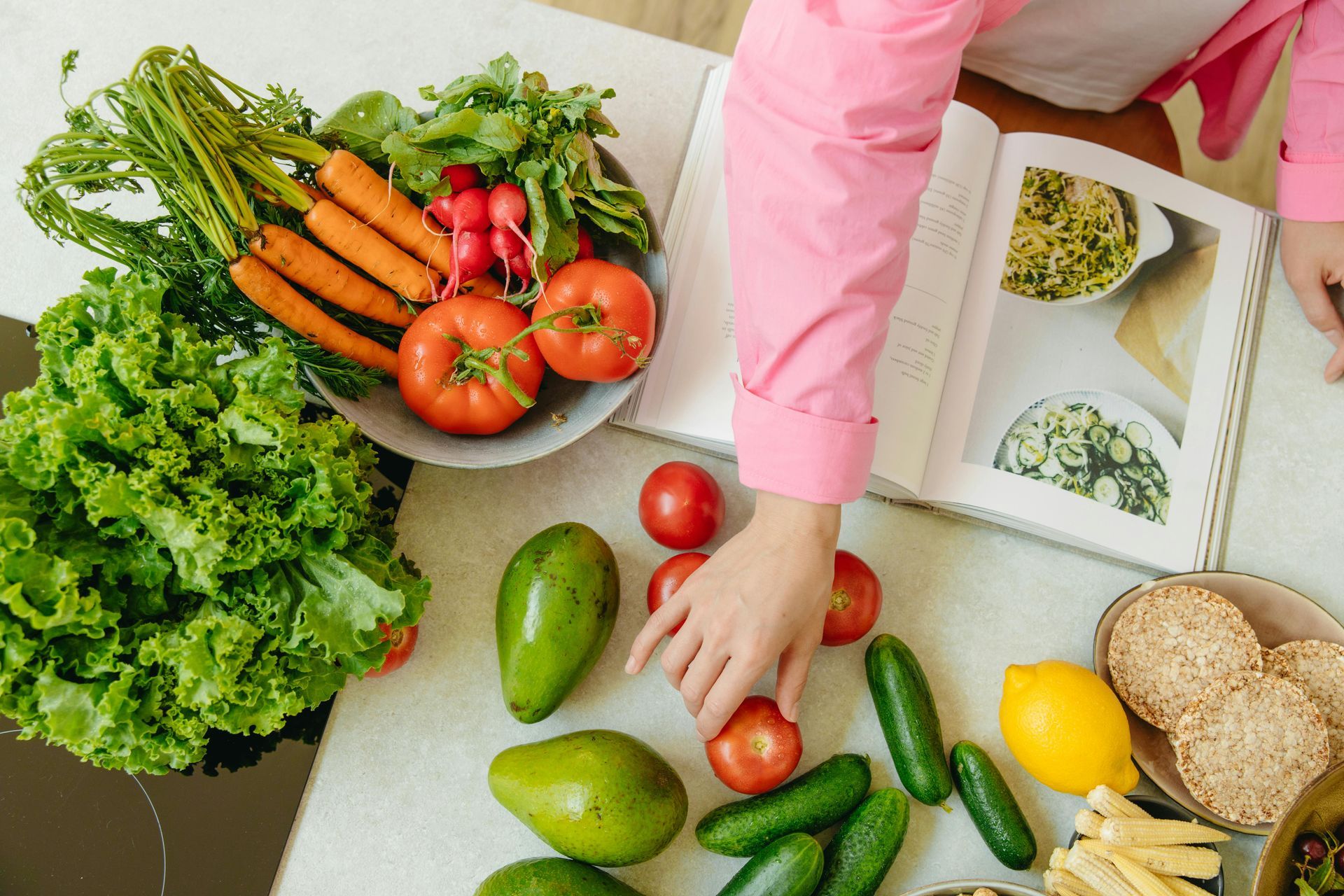 Person following a recipe from a cookbook, grabbing vegetables to make a dish