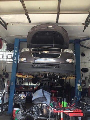 A car is sitting on a lift in a garage with the hood up.