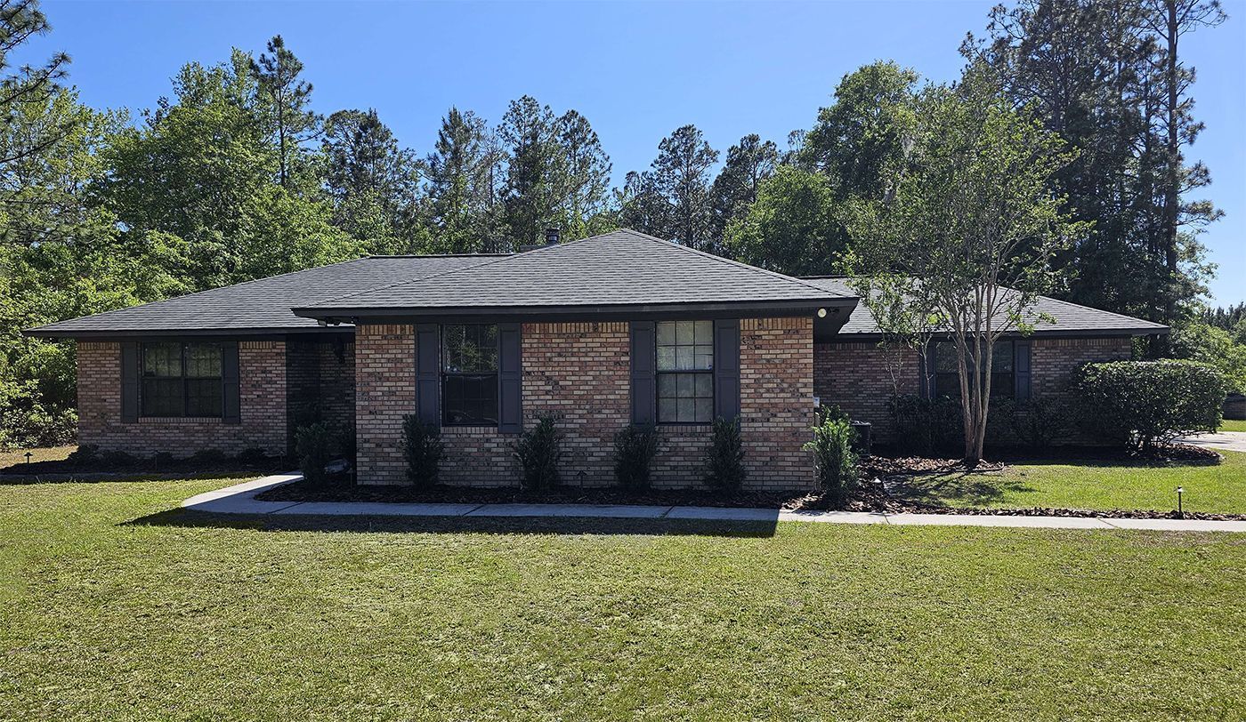 A brick house with a black roof is surrounded by trees and grass.